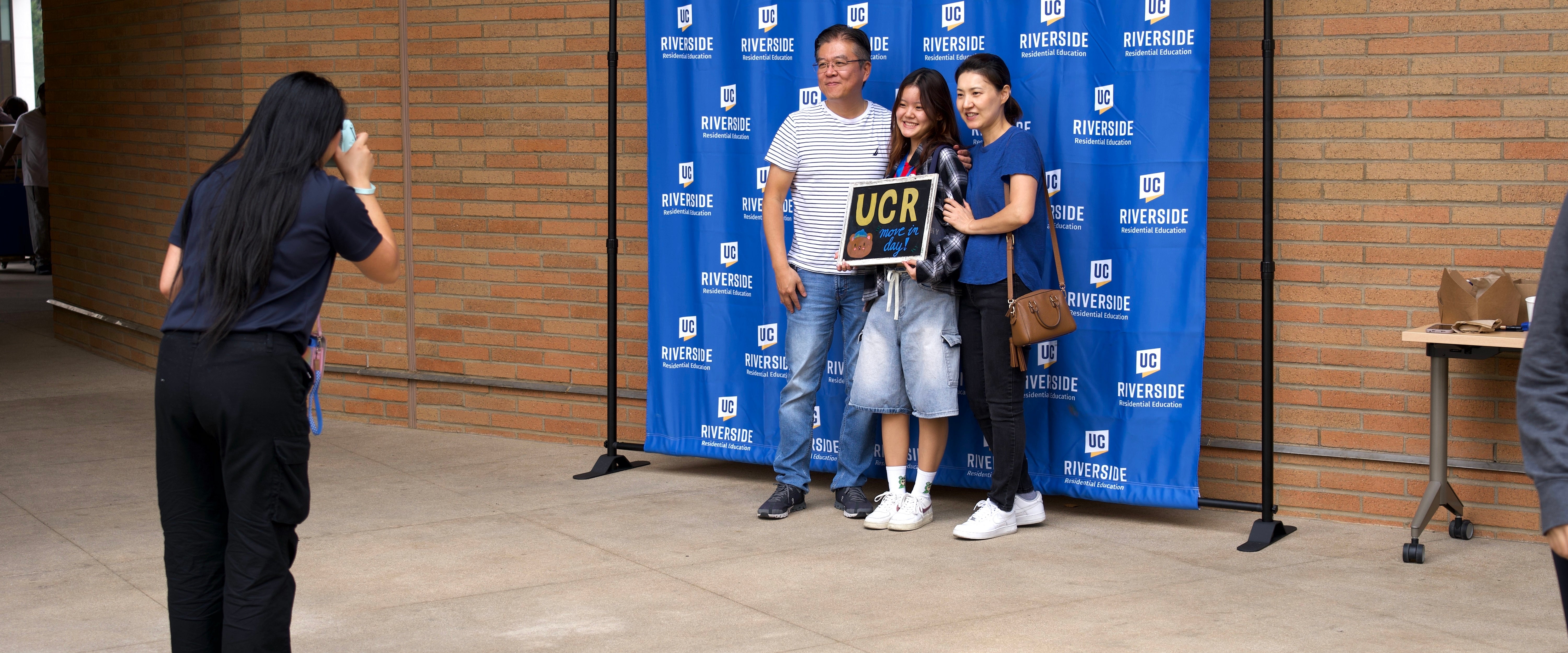 A new students takes a photo with their parents in front of a UCR backdrop on Move-In Day.